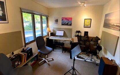 A photo of Chris's lesson room: a warm, lamplit room with a piano, electronic drumset and several pieces of art